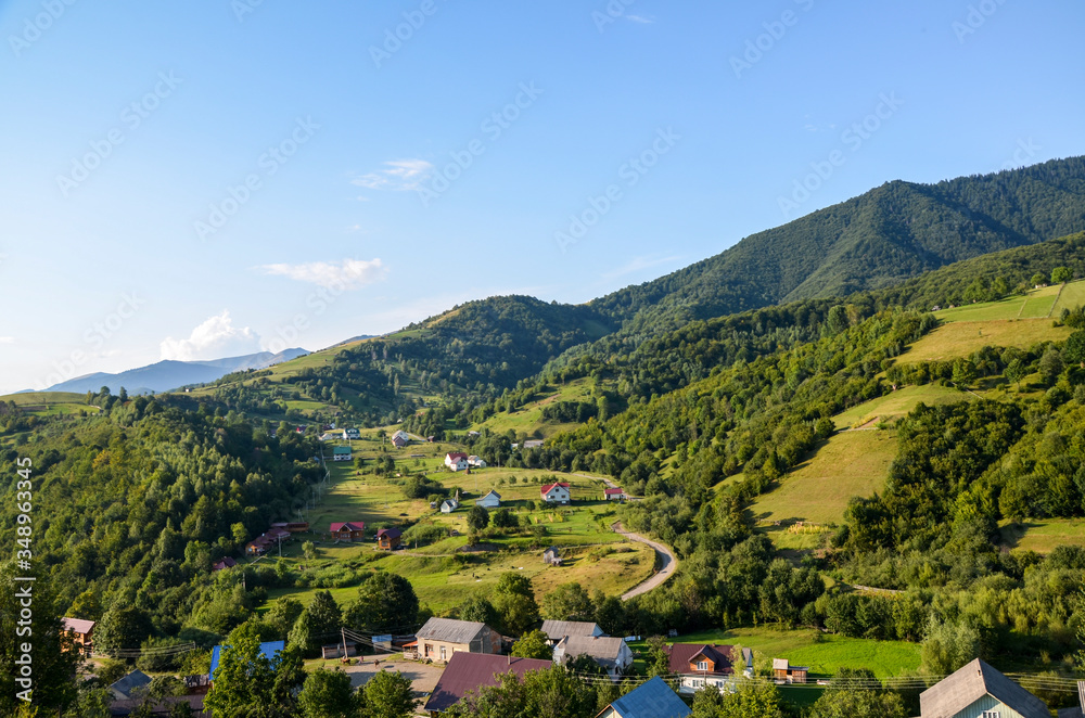 Carpathian mountain landscape with village houses on hills and green meadows in valley