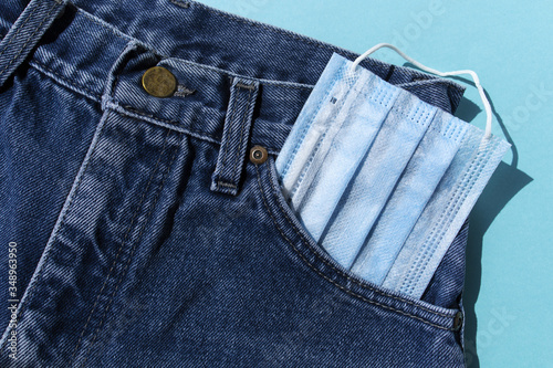 Classic blue jeans on the white background. Medical mask in the pocket. Pandemic concept. Top view. Flat layout