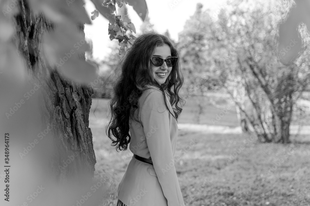 black and white photo. Fashion smiling portrait of girl posing on the park. Wearing stylish suit, sunglasses.