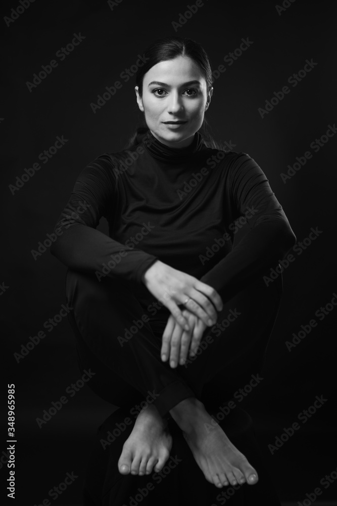 Cute young girl in black turtleneck and black pants sitting on chair and smiling