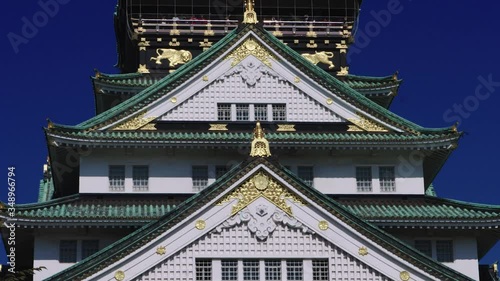 Detail of Osaka Castle in Japan with stunning blue sky behind and birds flying past. The roof is green with beautiful gold detail