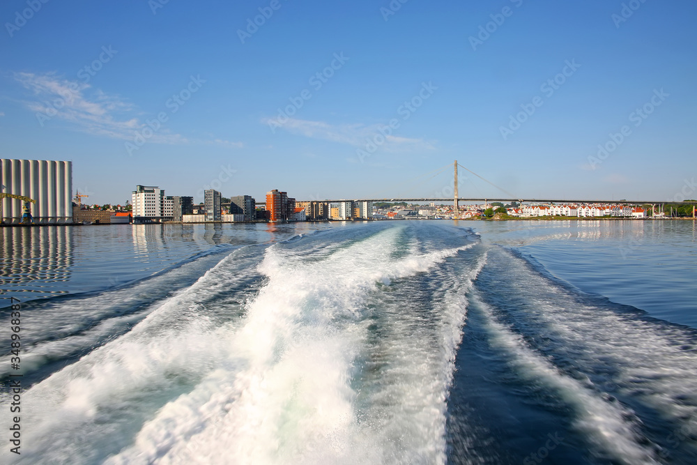 Waves in the ocean from a wake of a boat while sailing away from Stavanger harbour. City Bridge & port in the background, Stavanger, Rogaland county, Norway.