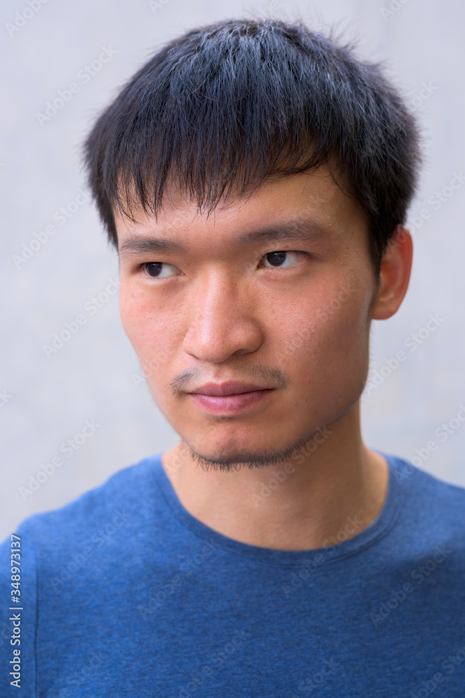 Face of young Asian man thinking against concrete wall Face of young Asian man thinking against concrete wall