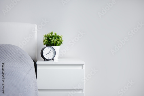 good morning concept - alarm clock and houseplant on bedside table and copy space over white wall