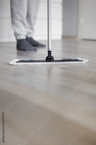 housekeeping concept - close up of man cleaning wooden floor with mop in living room - copy space over parquet