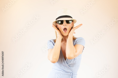 Young woman wearing hat and glasses making surprised gesture on vacation © Danko