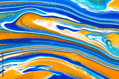 Fluid art texture. Background with abstract mixing paint effect. Liquid acrylic picture that flows and splashes. Mixed paints for baner or wallpaper. Blue, golden and white overflowing colors