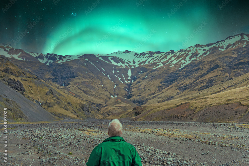 Man in green jacket are looking towards the highlands in Iceland and the snow covered mountains, the waterfalls with northern lights dancing above.