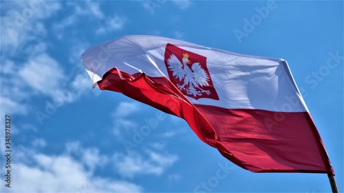 Polish flag waving in the wind. Blue sky in the background. Red, white and an eagle sign.