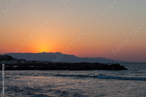 Sunset over the sea in Kokkini Hani, Crete, Greece. The sun disappears behind the mountain. Scenic seaside landscape in the evening.