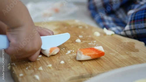Little babies' hands holding and learning to cut / slice crab sticks on a cutting board at home