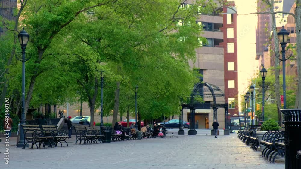 City street park lined with benches and people relaxing.