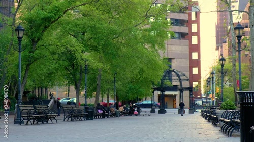 City street park lined with benches and people relaxing.