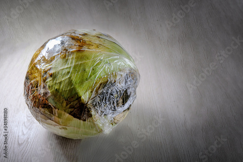 The cabbage is wrapped in cellophane. A spoiled vegetable. The concept of Ugly products, no plastic packaging. Copy space
