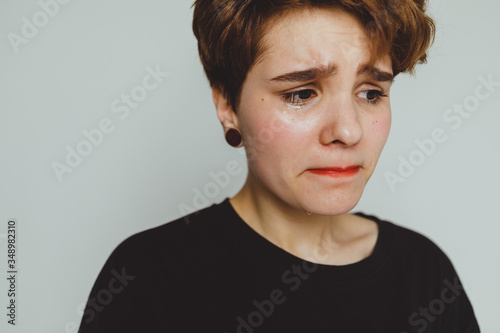Girl with short hair cries on a white background