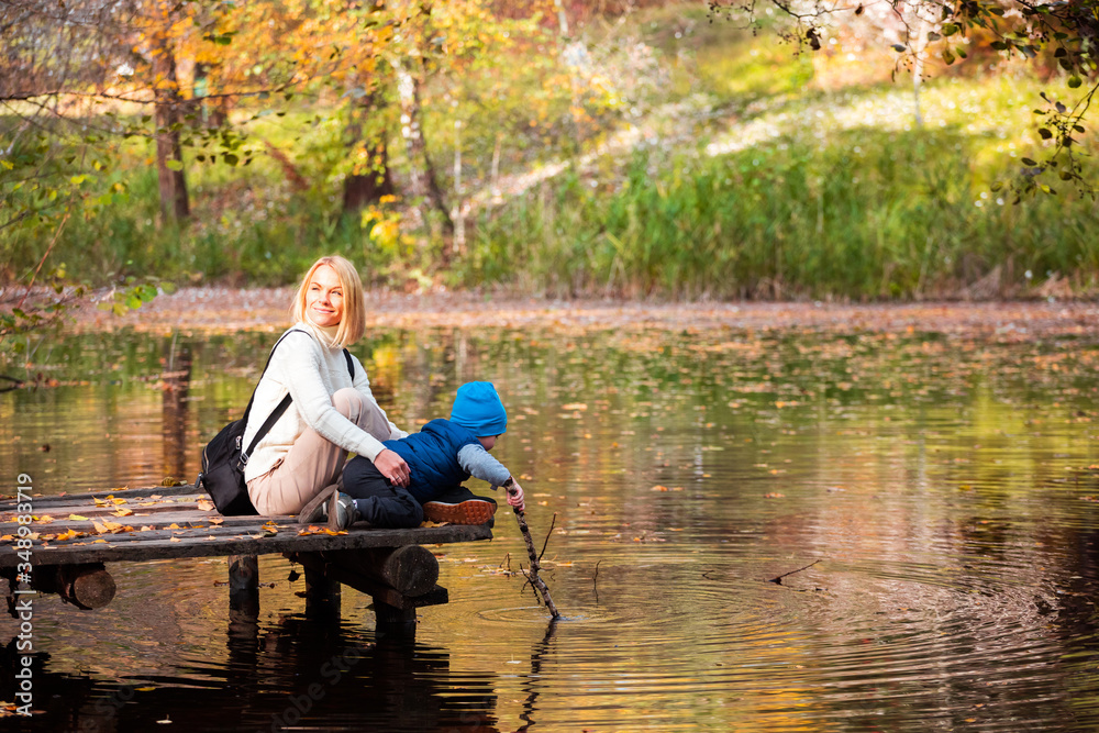 Happy young mother and her son spending time in the autumn park near the pond. Happy young mother and her son spending time in the autumn park near the pond.
