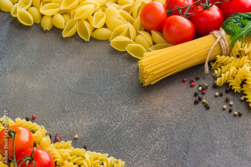 Frame with spaghetti and various ingredients for cooking pasta on a dark background, top view