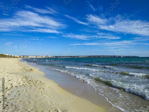 A wide sandy beach, the Mediterranean Sea with small waves and a bright blue sky. The deserted beaches of Spain are a crisis of international tourism.