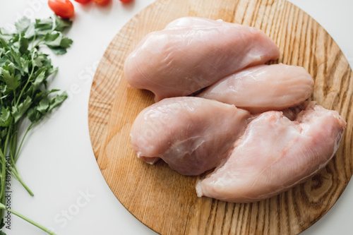 Chicken fillet on a wooden board with herbs, white background.