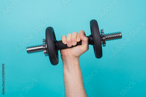 Working out concept. Cropped photo of a strong man holding dumbbell in hand isolated on blue background