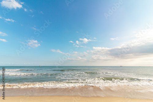 Beautiful tropical beach with sand, ocean wave against blue sky, clouds and horizon in sunny day. Nature and summer vacation concept.