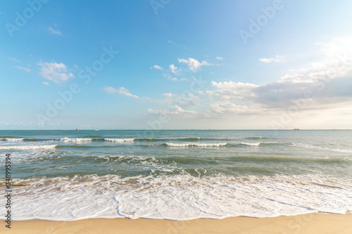 Beautiful tropical beach with sand, ocean wave against blue sky, clouds and horizon in sunny day. Nature and summer vacation concept.