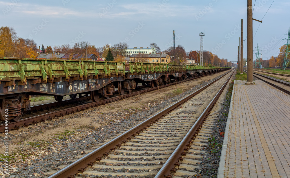 Landscape with railroad track and chain of old rusty green cargo wagons standing near platform.
