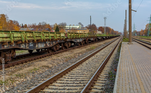 Landscape with railroad track and chain of old rusty green cargo wagons standing near platform.