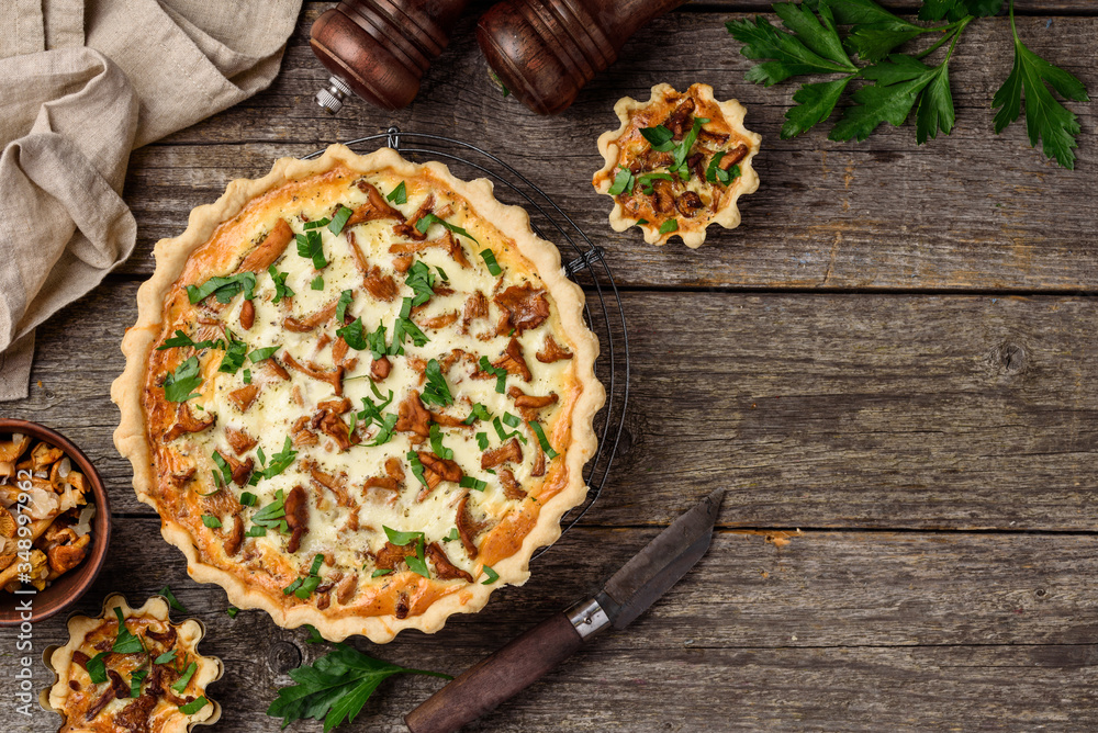 Homemade quiche or tart with chanterelles  and parsley on an old wooden background. A slice of tart on a plate. Rustic style. Top view.  Copy space - obrazy, fototapety, plakaty 