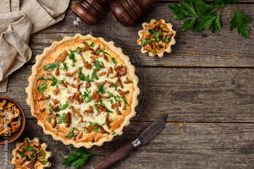Homemade quiche or tart with chanterelles and parsley on an old wooden background. A slice of tart on a plate. Rustic style. Top view. Copy space
