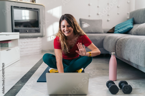 woman doing sports on a mat following online classes with laptop at home