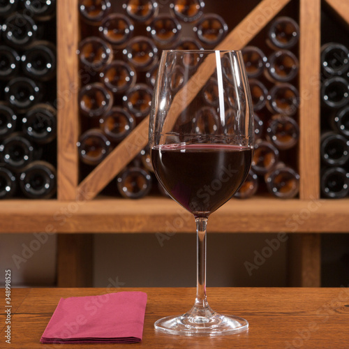 wine glass on a wooden table, against the background of a rack with many bottles of wine photo