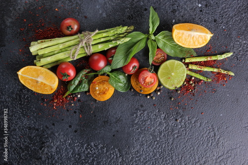 Fresh raw vegetables and herbs, asparagus, red cherry tomatoes, yellow tomatoes, lemon, lime, spinach, basil and spices on a black background. Top view, flatlay. Background image, copy space