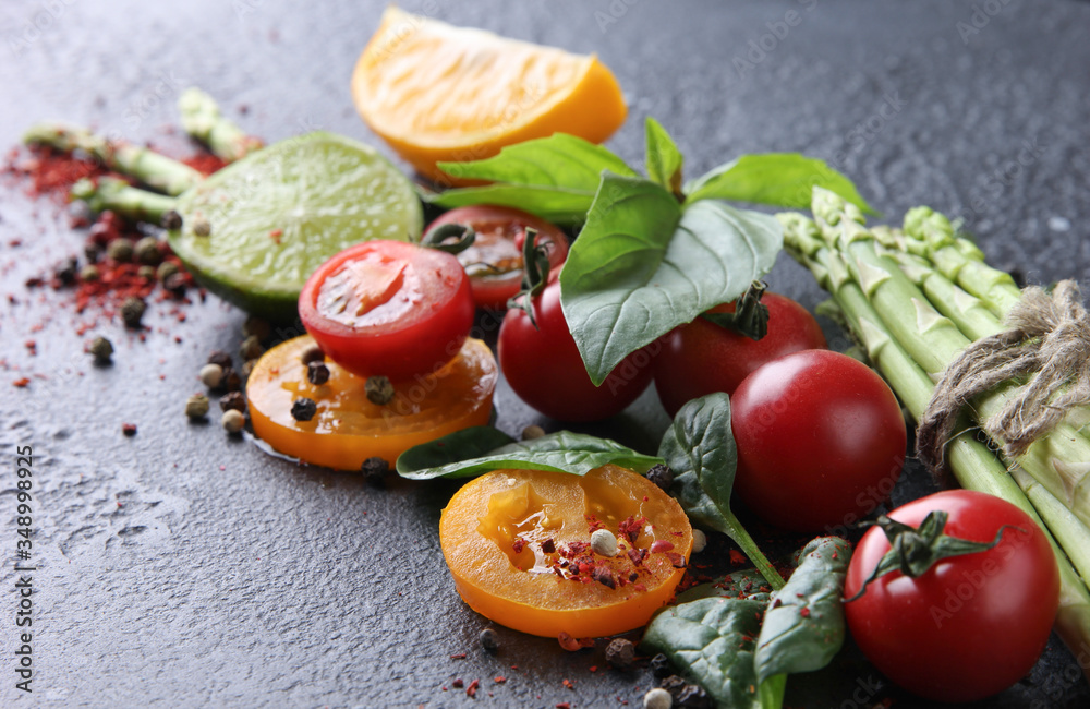 Fresh raw vegetables and herbs, asparagus, red cherry tomatoes, yellow tomatoes, lemon, lime, spinach, basil and spices on a black background. Background image, copy space