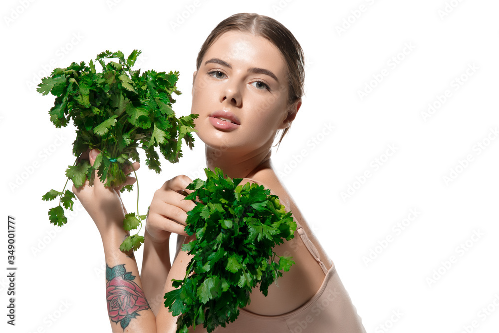 Close up of beautiful young woman with green leaves on her face over white background. Concept of cosmetics, makeup, natural and eco treatment, skin care. Shiny and healthy skin, fashion, healthcare.