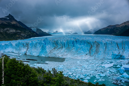 Ice wall of a glacier with some pieces of ice in the water in front of a forest © cristian