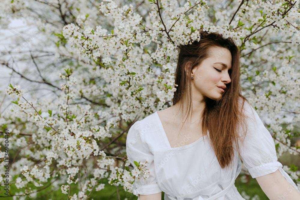 Portrait of a beautiful girl of European appearance in spring in a flowering garden near a flowering apple tree Portrait of a beautiful girl of European appearance in spring in a flowering garden near a flowering apple tree