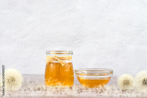 Dandelion jam, honey, jelly in a glass jar on a wooden table, white background with fresh flowers, dandelion airy seed heads, seeds, blow balls. Medicine, healthy food, health benefits from nature