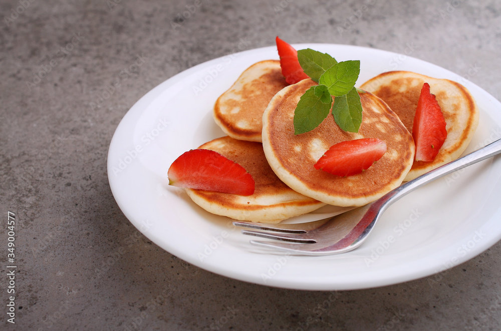 Pancake in a plate with strawberries decorated with mint on a concrete background