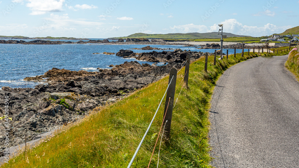 Shoreline road between fences with spectacular coastal scenery, sunny spring day with blue sky and white clouds on Inishbofin Island, County Galway, Ireland