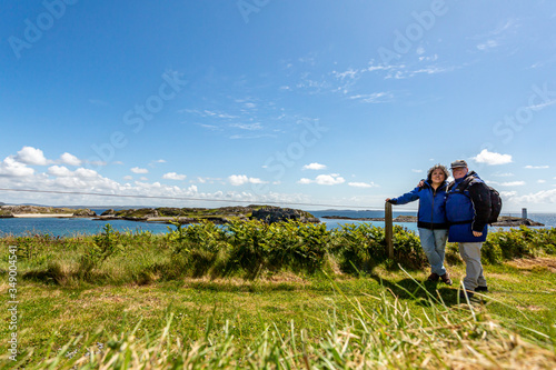 Tourist couple on a hill on Inishbofin or White Cow Island with the Atlantic Ocean in the background, sunny day on the small island off the coast of Connemara, County Galway, Ireland