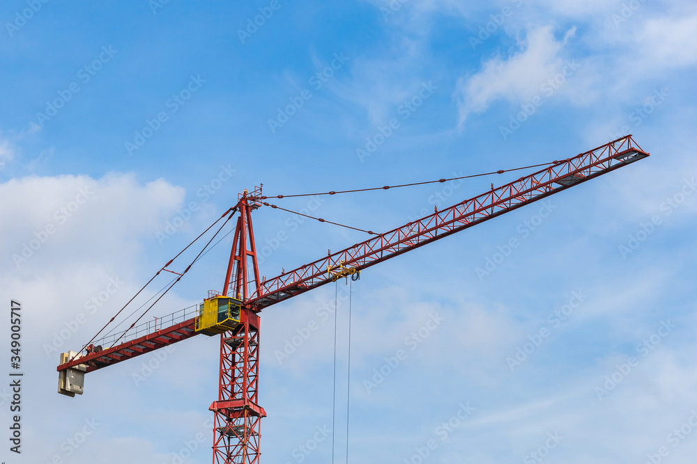 Red tower crane against light blue sky with white clouds. Close up. Copy space.