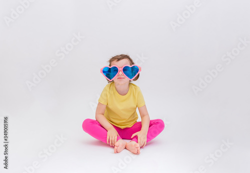 Cute funny girl sitting in big funny glasses on a white background place for text. A blonde girl in a yellow t-shirt and pink leggings. Day of laughter