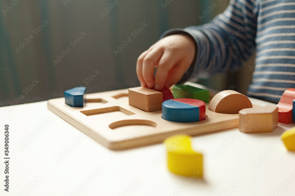 Educational toys, Cognitive skills, Montessori activity. Closeup: Hands of a little Montessori kid learning about color, shape, sorting, arranging by engaged colorful wooden sensorial blocks.
