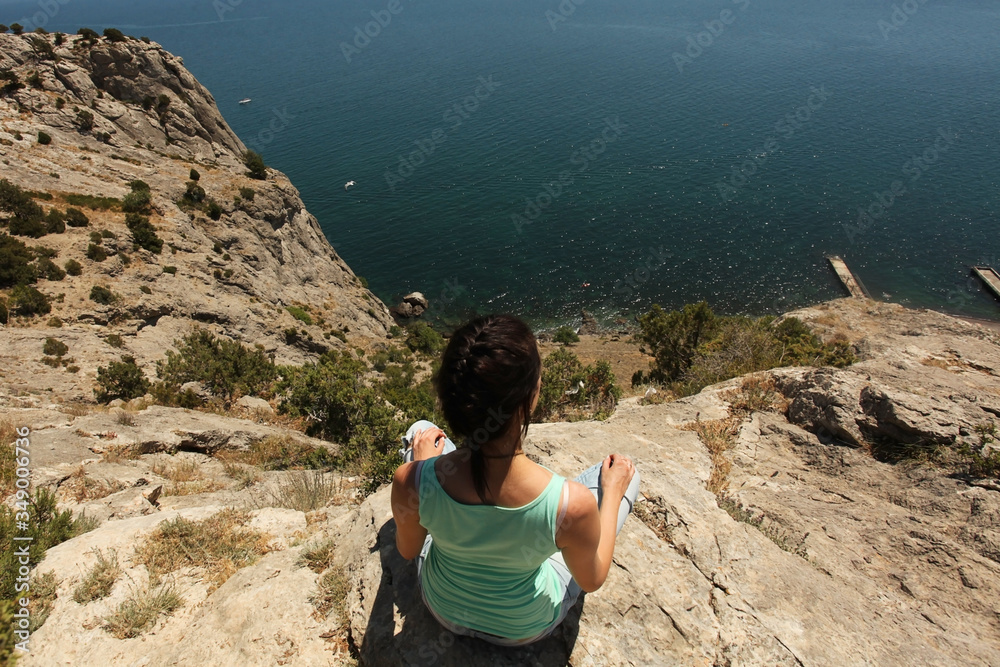 the girl sits on the edge of a cliff and looks out to sea. Meditation in the fresh air.