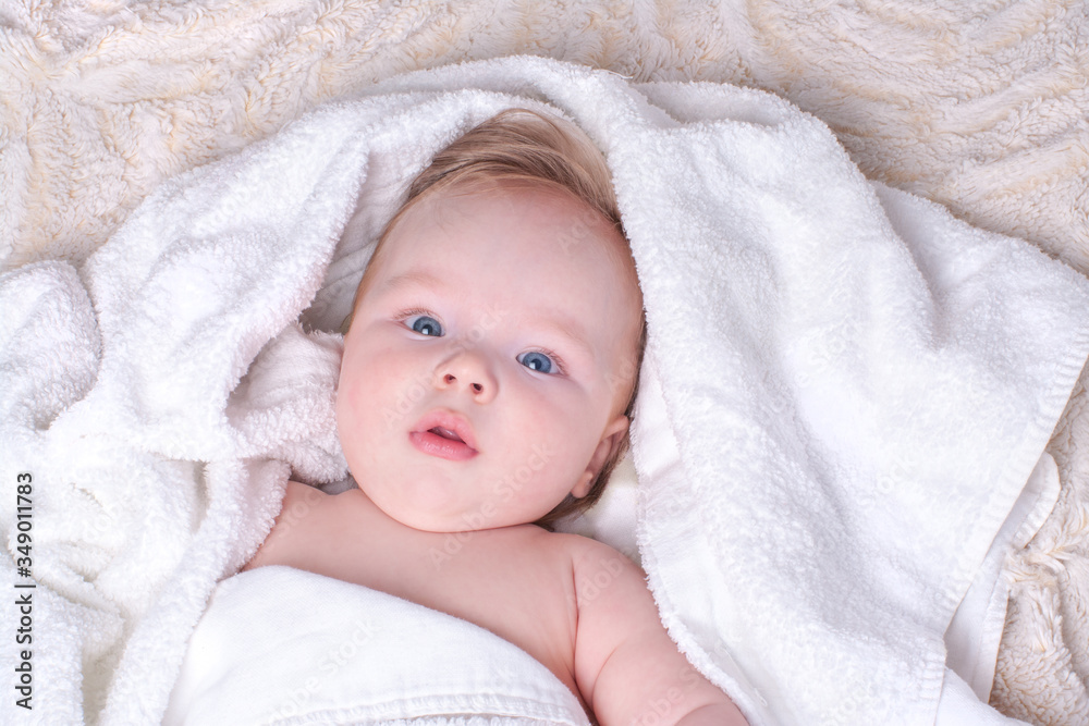 Surprised, newborn blue-eyed boy with plump lips and blond hair lies in dry, white towel on light fluffy blanket after bathing in bathroom. Textiles and bedding for children. Concept baby hygiene Surprised, newborn blue-eyed boy with plump lips and blond hair lies in dry, white towel on light fluffy blanket after bathing in bathroom. Textiles and bedding for children. Concept baby hygiene