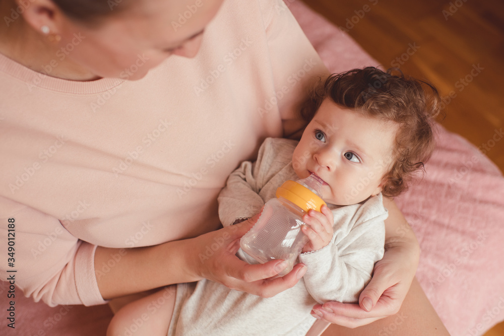 Baby girl under 1 year old drinking milk from bottle holding by mother. Healthy nutrition. Baby girl under 1 year old drinking milk from bottle holding by mother. Healthy nutrition.