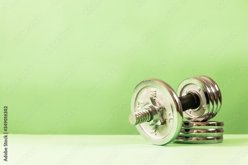 Large metal heavy dumbbell with pancakes on a green background with copy space Large metal heavy dumbbell with pancakes on a green background with copy space