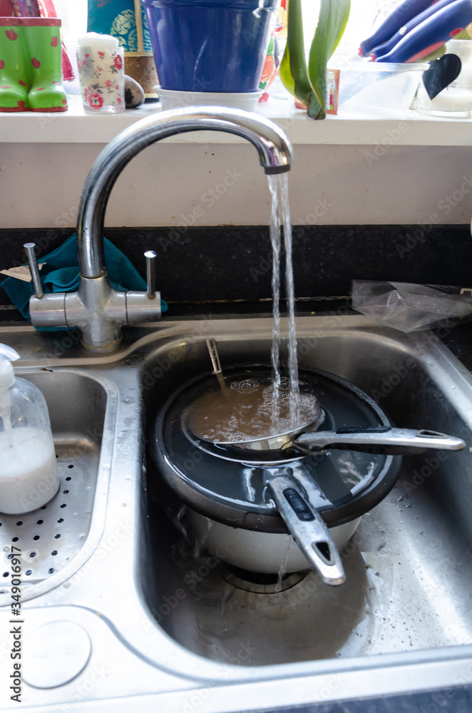 Obraz premium A running tap fills dirty pans with water so that they can soak in a kitchen sink to make them easier to clean.