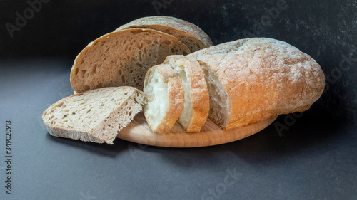 Beautiful bread close-up, two types of bread made from wheat and rye flour on a round wooden board on a black background. Sliced and half a loaf.